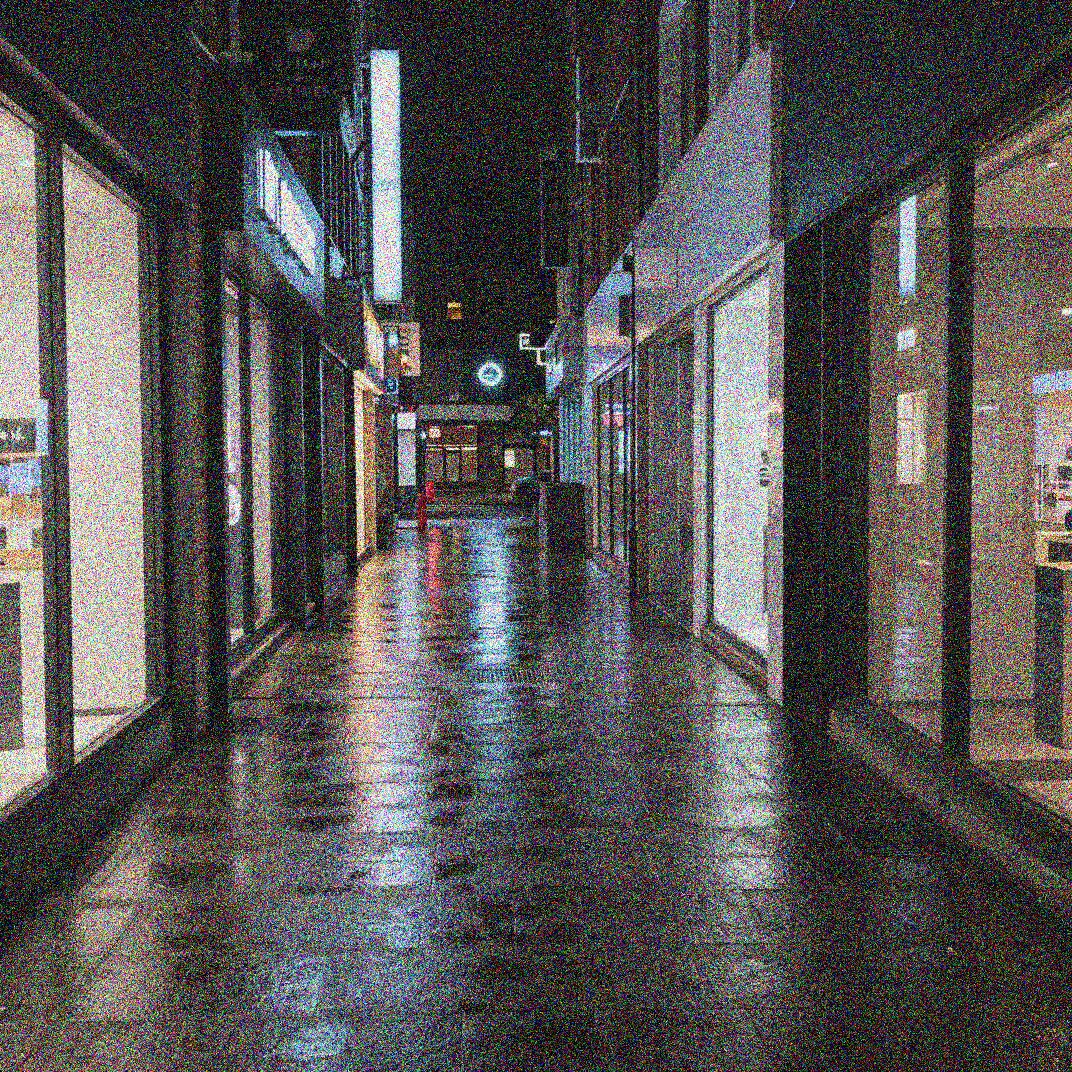 Grainy iPhone night photo of a city street with speckled shadows and noisy sky before AI noise reduction