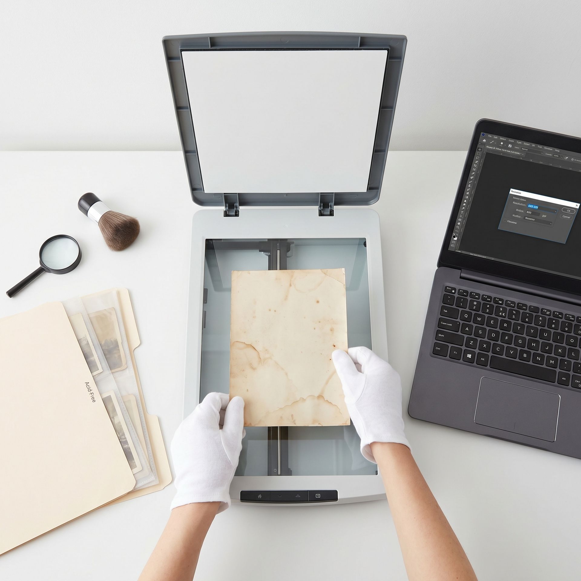 Overhead view of a flatbed scanner with a cleaned mold-damaged photograph being placed on the glass, laptop showing 600 DPI setting